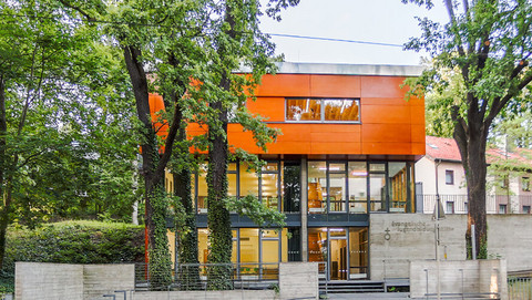 Modernes Tagungshaus mit orangefarbener Fassade zwischen hohen Bäumen