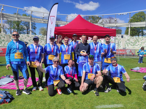 Laufteam in blauen Trikots posiert mit Medaillen für ein Gruppenfoto im Stadion